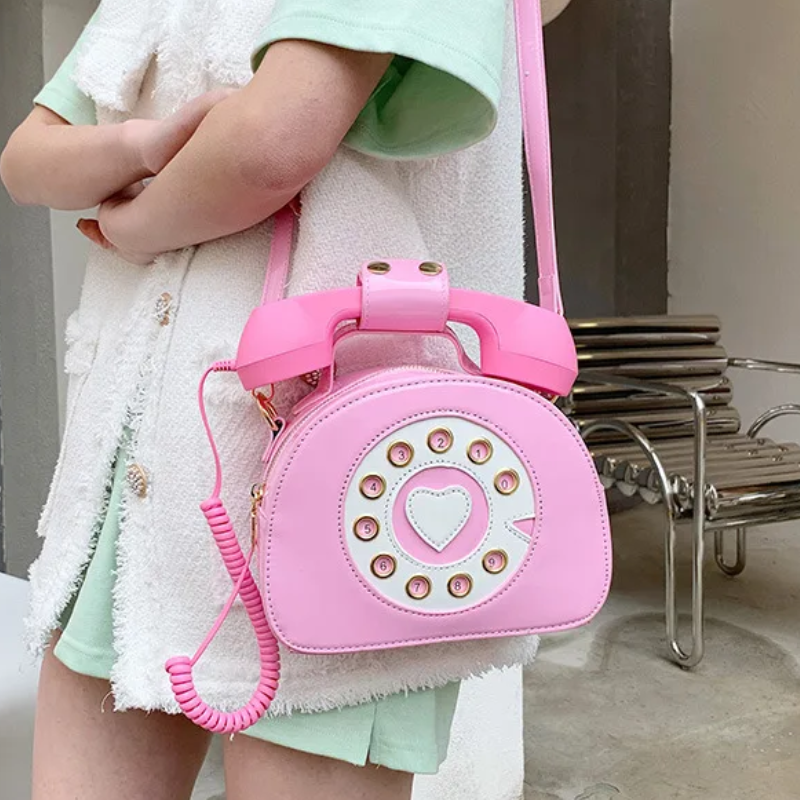 Pink kawaii shoulder bag in the shape of a telephone, featuring retro details and an adjustable strap, adding a fun and nostalgic touch to the look.