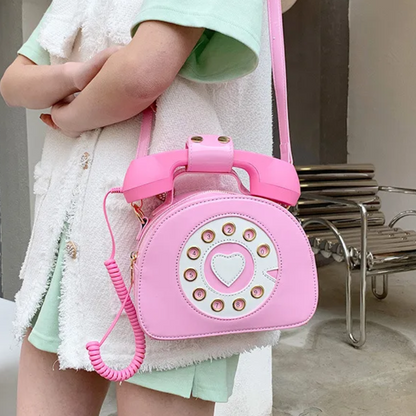Pink kawaii shoulder bag in the shape of a telephone, featuring retro details and an adjustable strap, adding a fun and nostalgic touch to the look.