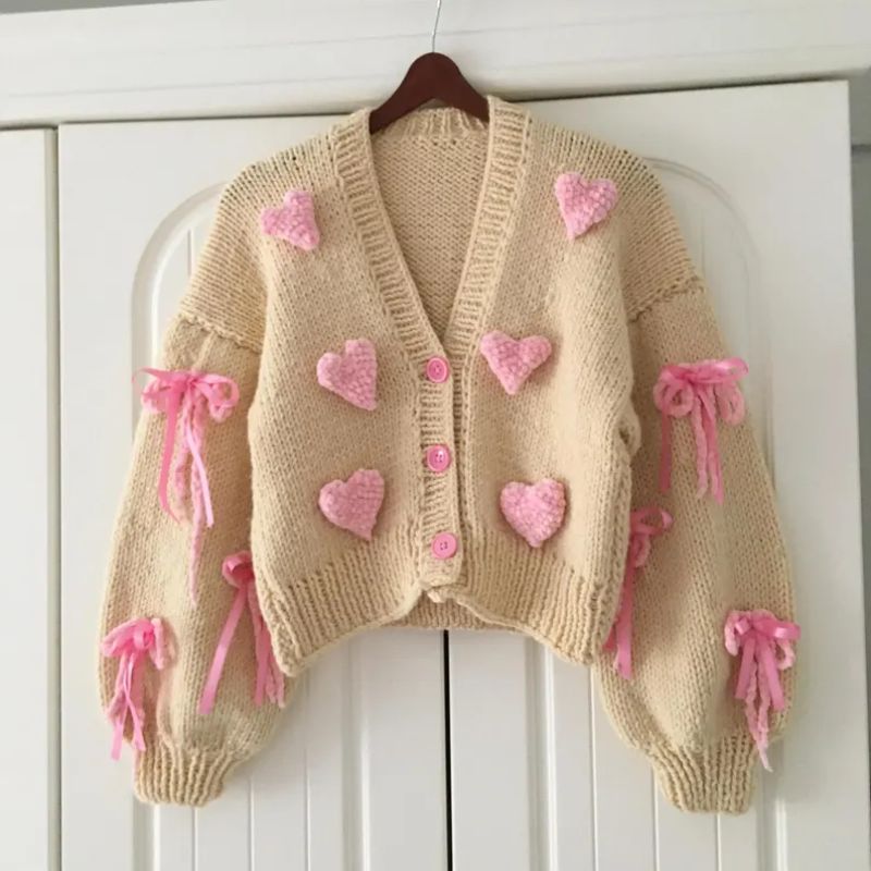 Short beige hand-knitted cardigan with pink hearts and bows